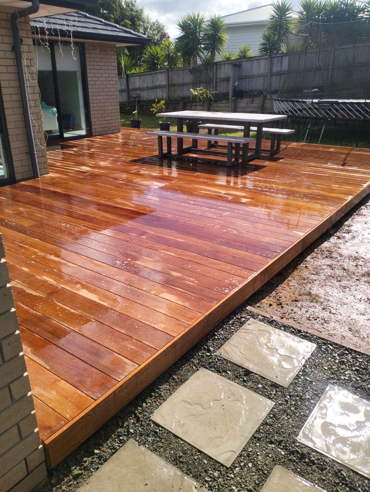 A wet timber deck beside a house, with outdoor furniture and stepping stones.