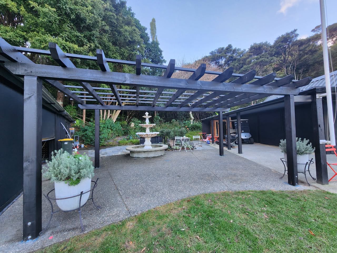 A dark timber pergola over a paved outdoor area with a central water feature.